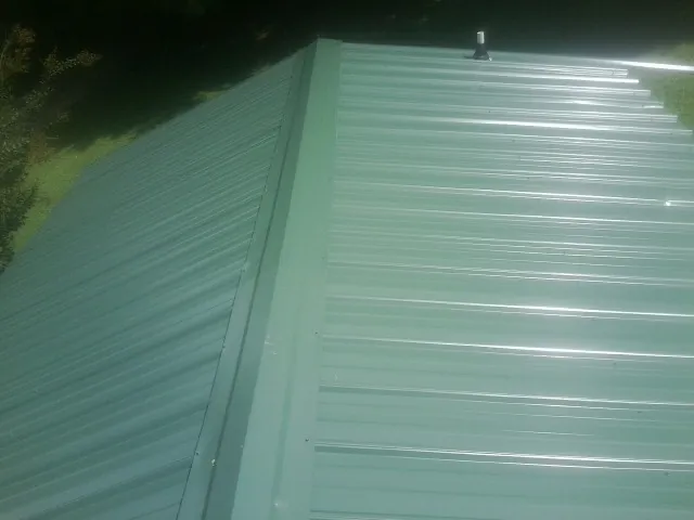 New green metal panels meeting at the ridge of a roof — Flat Roof Repair work by our crew in Tacoma