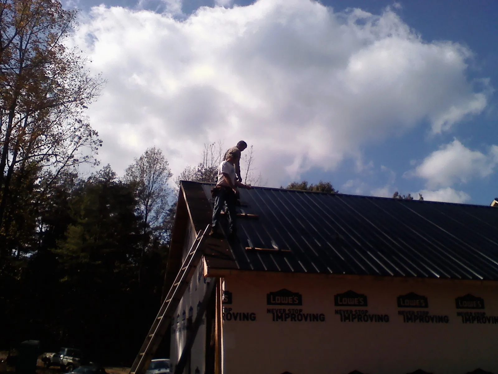 Roofer fastening dark metal panels high against a cloudy sky in Tacoma