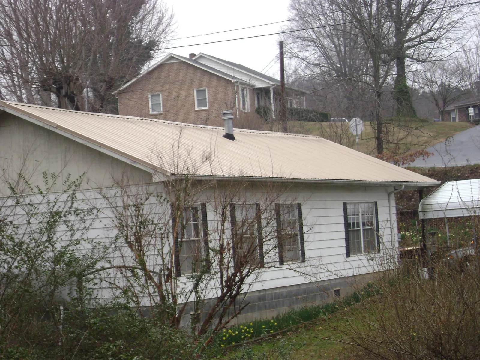 Tan metal roof on a white sided house set into a hillside — Commercial Roofing by Roofing Brothers in Tacoma